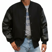 Load image into Gallery viewer, Person wearing a black varsity jacket with leather sleeves on a white background