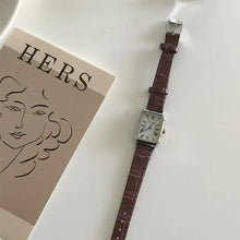 Load image into Gallery viewer, Vintage-inspired women's quartz watch with brown vegan leather strap and classic dial, styled on a white surface next to artistic print
