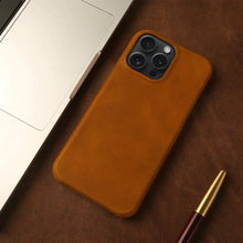 Cargar imagen en el visor de la galería, Genuine leather iPhone case with vintage aesthetic, brown color, shown on a desk beside a laptop and pen for elegant style