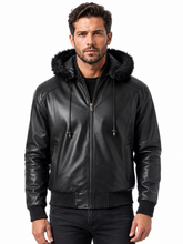 Cargar imagen en el visor de la galería, A man wearing a black faux-leather hooded jacket with a black faux-fur trimmed hood, black ribbed knit cuffs and hem, and a front zipper, photographed against a plain white background.