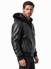 Cargar imagen en el visor de la galería, A man wearing a black faux-leather hooded jacket with a black faux-fur trimmed hood, ribbed knit cuffs and hem, and a front zipper, photographed against a plain white background.