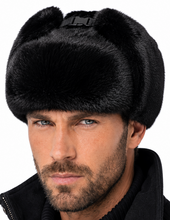 Load image into Gallery viewer, A man wearing a black faux fur ushanka winter hat with ear flaps and a black jacket against a white background.
