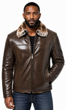 Cargar imagen en el visor de la galería, A man wearing a brown textured leather jacket with a brown faux-fur collar, paired with a black shirt and blue jeans, against a plain white background.