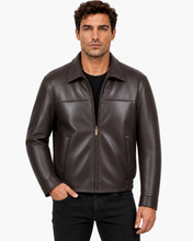 Charger l'image dans la galerie, A man wearing a dark brown leather jacket over a black shirt and black jeans, standing against a light gray studio background.