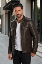Load image into Gallery viewer, A man wearing a dark brown leather jacket over a white t-shirt and black pants, standing on a city sidewalk.