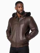 Load image into Gallery viewer, A man wearing a dark brown leather jacket with a fur trimmed hood, standing against a plain white background.