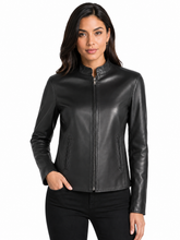 Cargar imagen en el visor de la galería, A woman modeling a black real-leather moto jacket with a stand collar and front zipper, paired with black pants, against a plain white background.