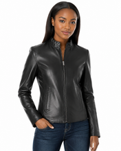 Cargar imagen en el visor de la galería, A woman modeling a black real-leather moto jacket with a stand collar and front zipper, paired with dark blue jeans, against a plain white background.