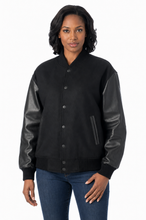Load image into Gallery viewer, A woman modeling a black varsity-style jacket with black real-leather sleeves, shown against a plain white studio background.