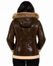 Cargar imagen en el visor de la galería, A woman viewed from the back wearing a glossy dark brown real-leather hooded jacket with a tan faux-fur trimmed hood and hem, paired with black pants, against a plain white background.