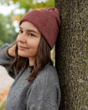 Charger l'image dans la galerie, Woman wearing CS105 HAAKWEAR Traditional Silent Cuffed Beanie, Rusty Burgundy, leaning against a tree in autumn setting.