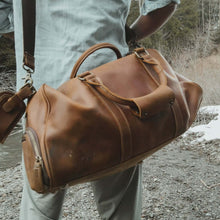 Load image into Gallery viewer, Traveler with The Dagny Weekender | Large Leather Duffle Bag in rustic outdoor setting.