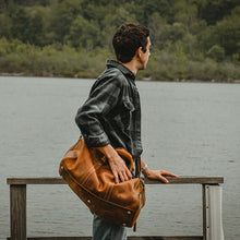 Load image into Gallery viewer, Man standing by lake with The Dagny Weekender | Large Leather Duffle Bag over shoulder
