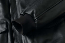 Load image into Gallery viewer, Close-up of a black leather aviator bomber jacket sleeve with knit cuff and pocket, highlighting the luxury and durability of REED.