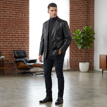 Load image into Gallery viewer, Man in a black suit standing in a modern room with brick walls and a plant.