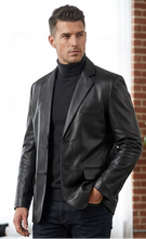 Charger l'image dans la galerie, Man in a black suit standing in a modern room with brick walls and a plant.