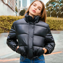 Load image into Gallery viewer, Woman wearing a thick black PU leather coat, showcasing winter fashion and style against an urban backdrop.