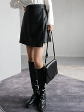 Load image into Gallery viewer, Woman wearing high-waist PU leather A-line split skirt in black with matching boots and handbag, showcasing stylish and trendy look.