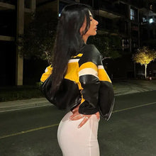 Charger l'image dans la galerie, Woman wearing a patchwork vegan leather jacket in black and yellow, standing stylishly on a nighttime city street.