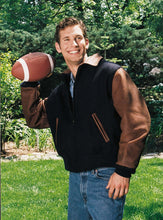 Load image into Gallery viewer, Man wearing REED Executive Varsity Jacket with leather cowhide sleeves and wool body, holding a football outdoors in a garden setting.