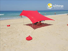 Load image into Gallery viewer, eZthings UV Sun Shade Beach Shelter in red, providing sun protection on a sandy beach with visible sandbag anchors.