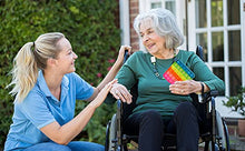 Load image into Gallery viewer, Woman in wheelchair holding eZthings stress relief fidget toy, assisted by caregiver in garden setting.