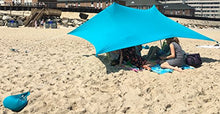 Load image into Gallery viewer, UV light sun shade beach shelter with sandbag anchors providing protection from harmful UV rays on a sandy beach.