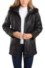 Load image into Gallery viewer, Women&#39;s black lamb leather jacket with detachable fox fur hood and braided trim, worn over a white top, stylish winter fashion.
