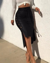 Load image into Gallery viewer, Woman in white top wearing a black high-waist faux leather midi skirt with side buttons and belt, standing against a white wall
