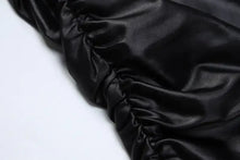Cargar imagen en el visor de la galería, Close-up of black faux leather fabric with ruched detailing, showcasing the sleek texture of the Be So Faux Real Mini Dress.
