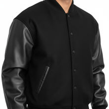 Cargar imagen en el visor de la galería, Black varsity jacket with leather sleeves on a white background
