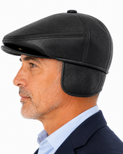 Load image into Gallery viewer, A man in profile wearing a black leather flat cap with attached ear flaps, shown against a clean white background.
