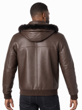Load image into Gallery viewer, A man viewed from the back wearing a brown real-leather hooded jacket with a dark faux-fur collar and ribbed knit trim, paired with dark jeans against a plain white background.
