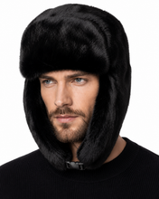 Load image into Gallery viewer, A man wearing a black faux fur ushanka hat with ear flaps and a chin strap, shown against a plain white background.
