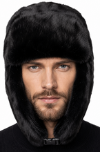 Load image into Gallery viewer, A man wearing a black faux fur ushanka winter hat with ear flaps and a chin strap, shown against a plain white background.
