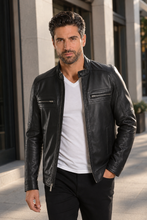 Load image into Gallery viewer, A man wearing a black leather motorcycle jacket over a white t-shirt and black pants, standing outdoors in front of a modern building.
