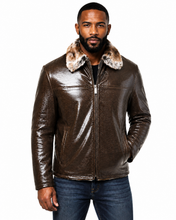 Load image into Gallery viewer, A man wearing a brown textured leather jacket with a fluffy beige and brown fur collar, paired with blue jeans, against a plain white background.

