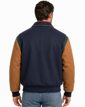 Load image into Gallery viewer, A man wearing a color-blocked wool-blend bomber jacket with a navy blue body, tan sleeves, and green shoulder panels, paired with blue jeans against a white studio background.
