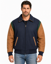 Load image into Gallery viewer, A man wearing a colorblock zip-up jacket with navy blue body, tan sleeves, and green shoulder panels, paired with blue jeans, against a plain white background.
