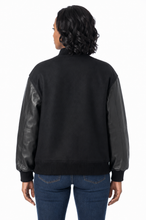 Cargar imagen en el visor de la galería, A person shown from the back wearing a black knit jacket with dark real-leather sleeves, paired with blue jeans, against a plain white background.
