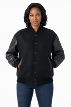 Cargar imagen en el visor de la galería, A woman modeling a black varsity-style jacket with black leather sleeves and black denim jeans, shot against a plain white background.
