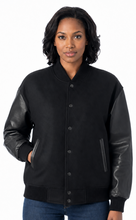 Cargar imagen en el visor de la galería, A woman wearing a black varsity-style jacket with black leather-look sleeves, paired with blue jeans, against a plain white background.
