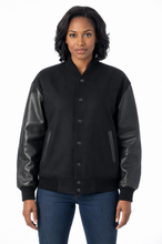 Cargar imagen en el visor de la galería, A woman wearing a black varsity-style jacket with black real-leather sleeves, ribbed knit collar and cuffs, and front buttons, paired with blue jeans against a plain white background.
