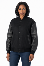 Cargar imagen en el visor de la galería, A woman wearing a black varsity-style jacket with black real-leather sleeves, shown against a plain white studio background.
