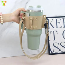 Load image into Gallery viewer, Leather coffee cup carrier with shoulder strap in beige, holding a green travel mug, ideal for hands-free convenience.
