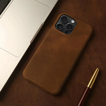 Cargar imagen en el visor de la galería, Vintage aesthetic genuine leather iPhone case on desk next to laptop and pen, showcasing sophisticated phone accessory.

