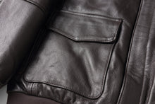 Charger l'image dans la galerie, Close-up of a dark brown textured leather jacket showing a flap pocket and the rich leather grain.
