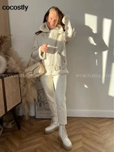 Load image into Gallery viewer, Woman wearing a white faux leather fur coat with a hood, standing in a sunlit room with a handbag.
