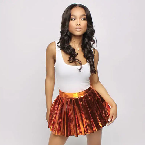 Model wearing chic pleated faux leather mini skirt in metallic orange, paired with a white top, showcasing playful and sophisticated style.
