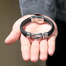 Load image into Gallery viewer, Men&#39;s leather bracelet with bold graphics and &quot;Te Amo&quot; engraving displayed on open hand.
